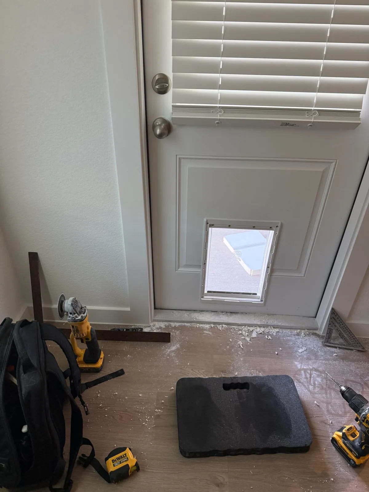 White exterior door with a newly installed pet door and tools nearby during installation
